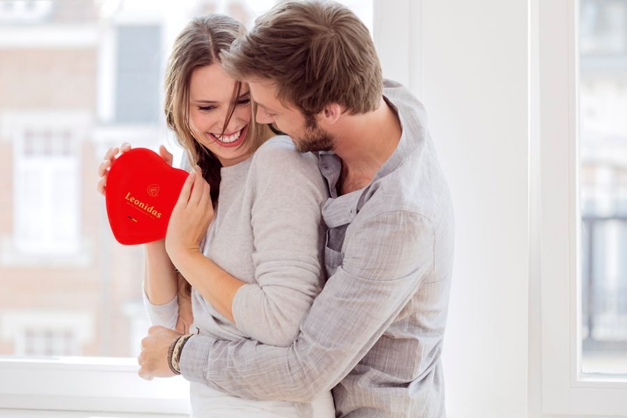 A couple holding a red heart-shaped box of Leonidas chocolates