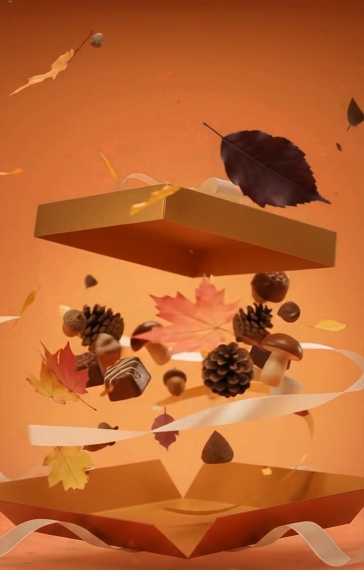 An open gold gift box with chocolates, chocolate mushrooms, acorns, pine cones and autumn leaves held in the air above it
